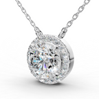 A round diamond pendant necklace with a halo setting and a central round-cut diamond, suspended from a delicate silver-toned chain against a white background.