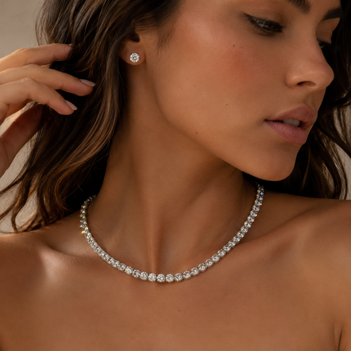 Woman wearing a diamond necklace and earrings with a neutral background