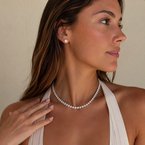 Woman wearing a pearl necklace and diamond earrings against a neutral background