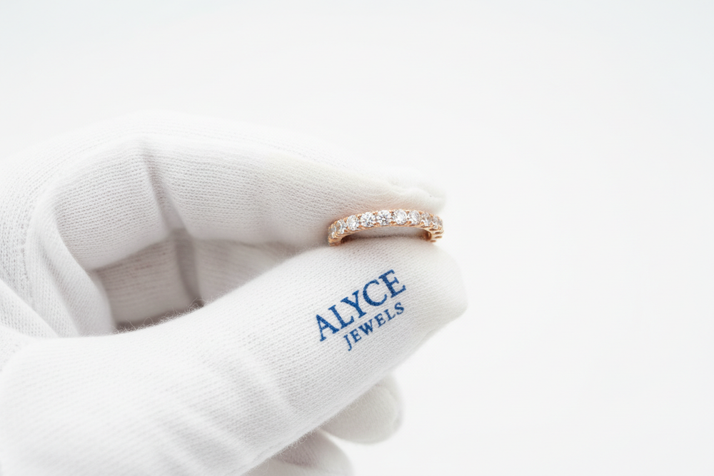8K detailed shot of a rose gold eternity band held with white gloves featuring a blue serif ‘Alyce Jewels’ logo on it. Bright stones and smooth lighting.