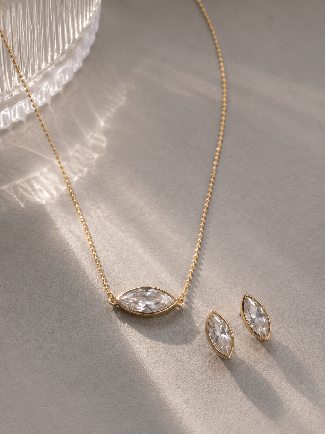 Gold necklace and earrings with clear stones on a textured surface