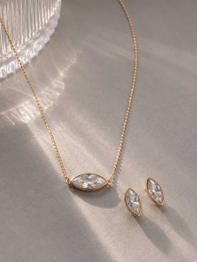 Gold necklace and earrings with clear stones on a textured surface