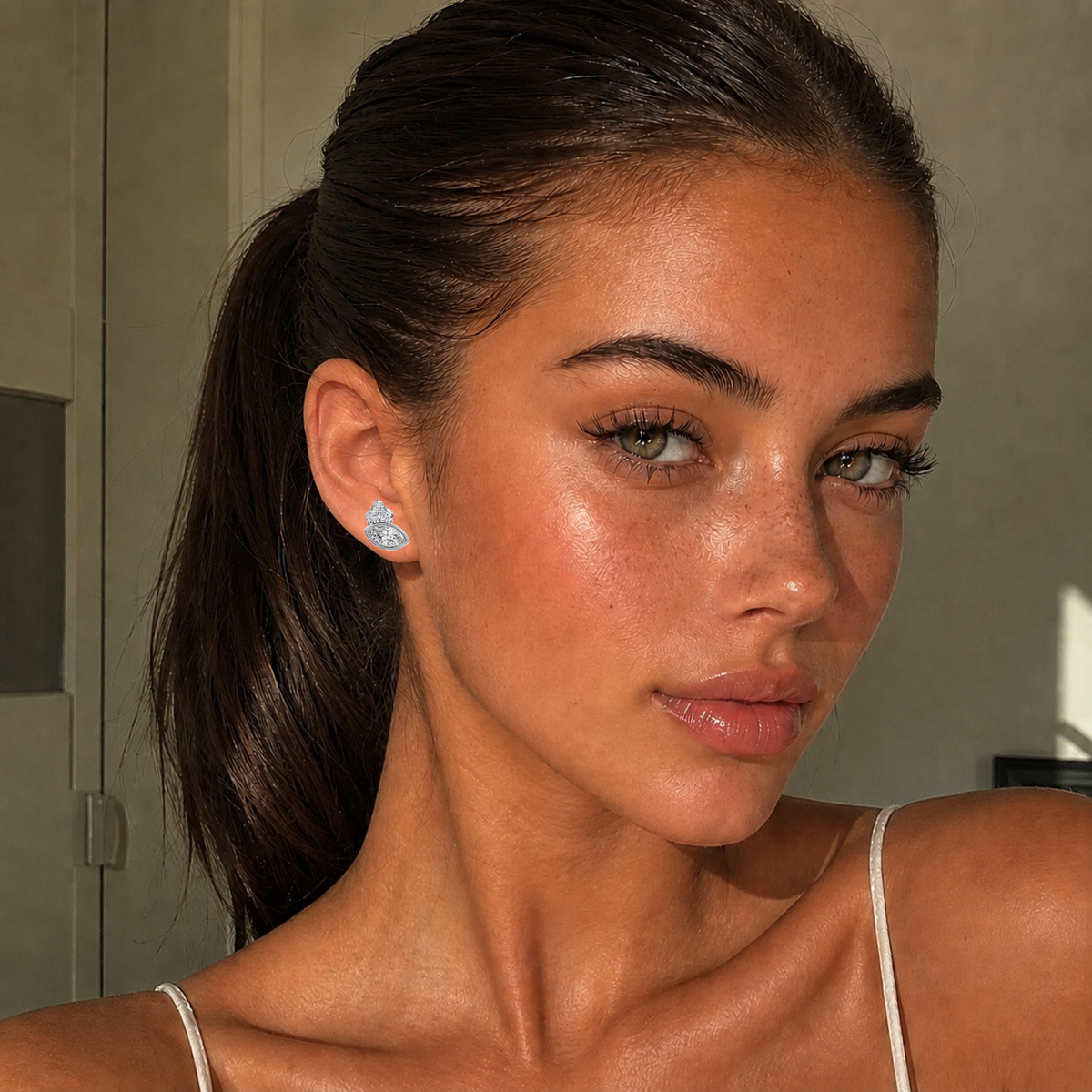 Woman with a ponytail wearing earrings, with a neutral background