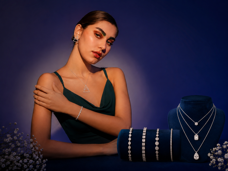 Woman wearing a green dress with jewelry, including necklaces and earrings, against a dark blue background.