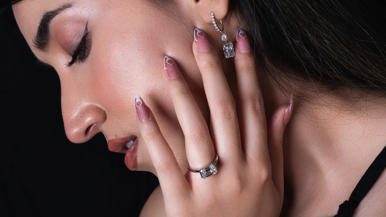 Close-up of a woman wearing diamond earrings and ring against a dark background