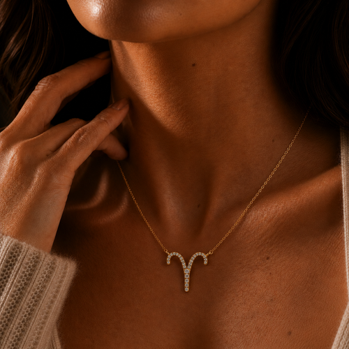 Person wearing a gold Aries zodiac necklace on a neutral background