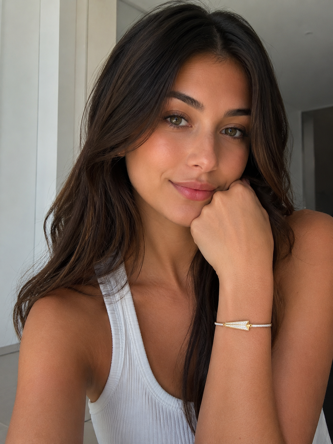 Woman wearing a white sleeveless top with a gold bracelet, indoors.
