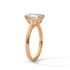 Angled side view of an emerald cut diamond solitaire engagement ring in rose gold with a raised four-prong setting and plain band.
