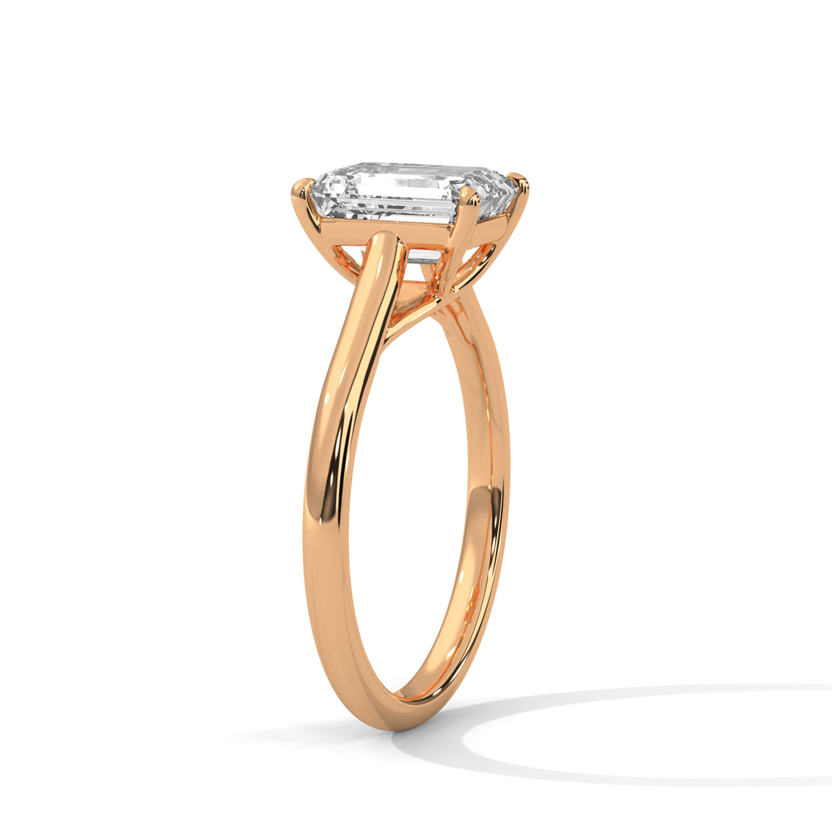 Angled side view of an emerald cut diamond solitaire engagement ring in rose gold with a raised four-prong setting and plain band.