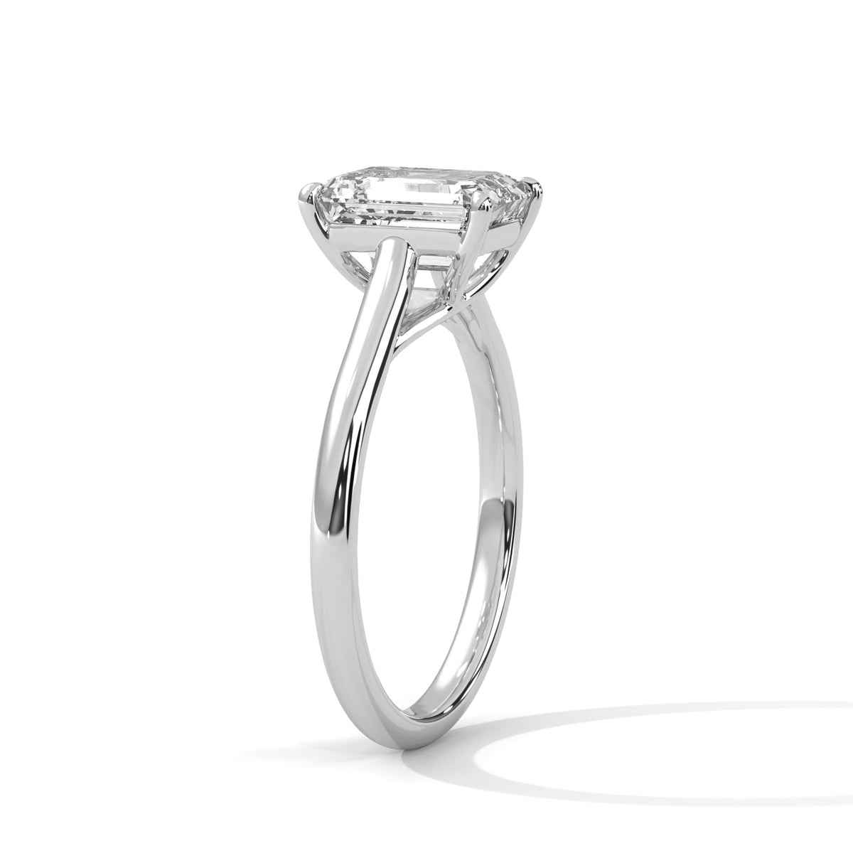Angled side view of an emerald cut diamond solitaire engagement ring in white gold with a raised four-prong setting and plain band.