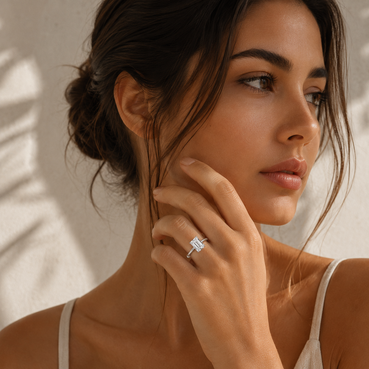 Woman wearing an emerald cut diamond solitaire engagement ring in white gold in a close-up lifestyle hand pose.