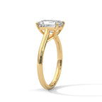 Angled side view of an emerald cut diamond solitaire engagement ring in yellow gold with a raised four-prong setting and plain band.