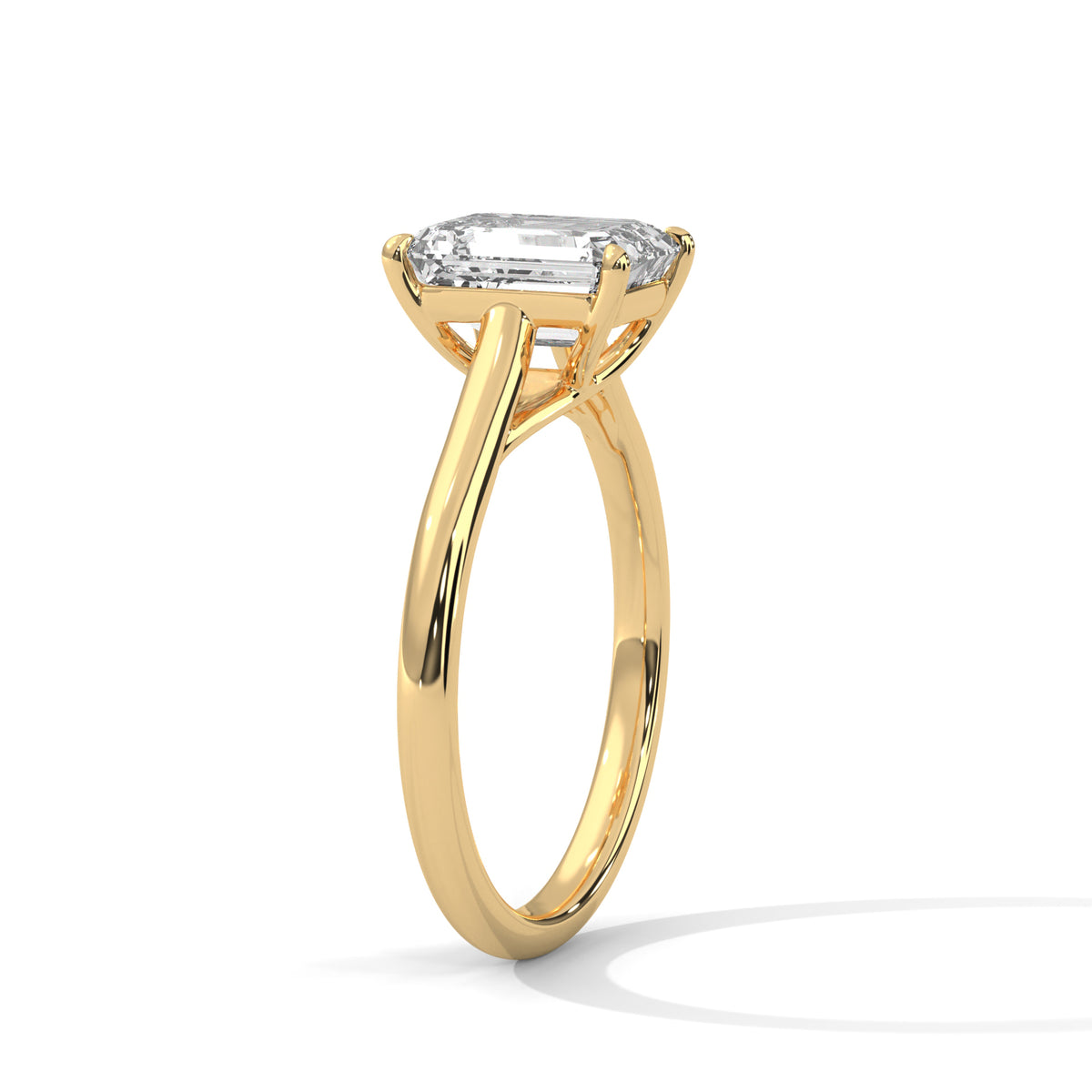 Angled side view of an emerald cut diamond solitaire engagement ring in yellow gold with a raised four-prong setting and plain band.