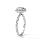 Angled side view of an oval cut diamond halo engagement ring in white gold with a pavé diamond band and raised halo setting.