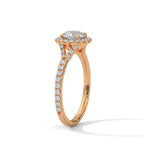 Angled side view of a round cut diamond halo engagement ring in rose gold with a pavé diamond band and diamond-accented gallery.
