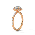 Angled side view of a round cut diamond halo engagement ring in rose gold with a pavé diamond band and raised halo setting.