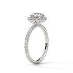 Angled side view of a round cut diamond halo engagement ring in white gold with a pavé diamond band and raised halo setting.