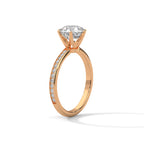 Side angle of a round cut diamond engagement ring in rose gold with a raised prong setting and pave diamond band.