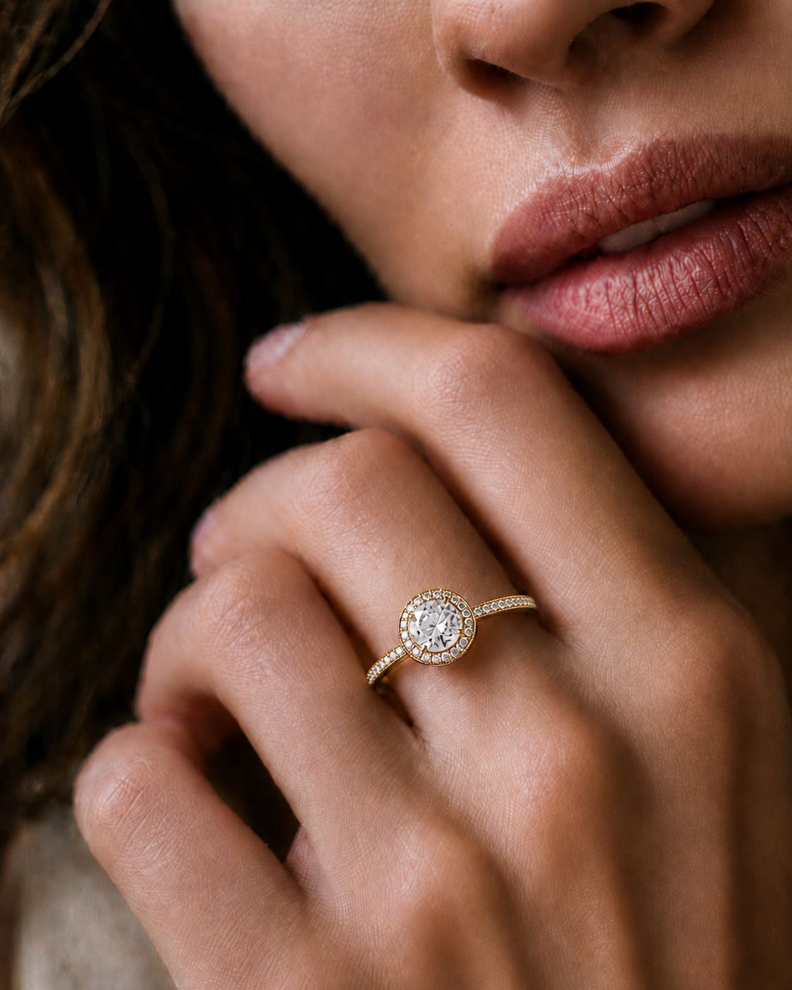 Woman wearing a round cut diamond halo engagement ring in yellow gold with a pavé diamond band in a close-up hand pose.